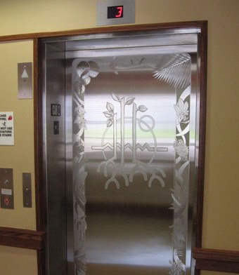 Etched stainless steel elevator doors showing island plants around a central circular mandala