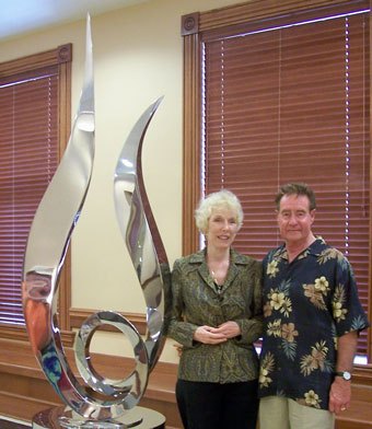 Two tall polished stainless steel curved forms standing together indoors, with two people beside them