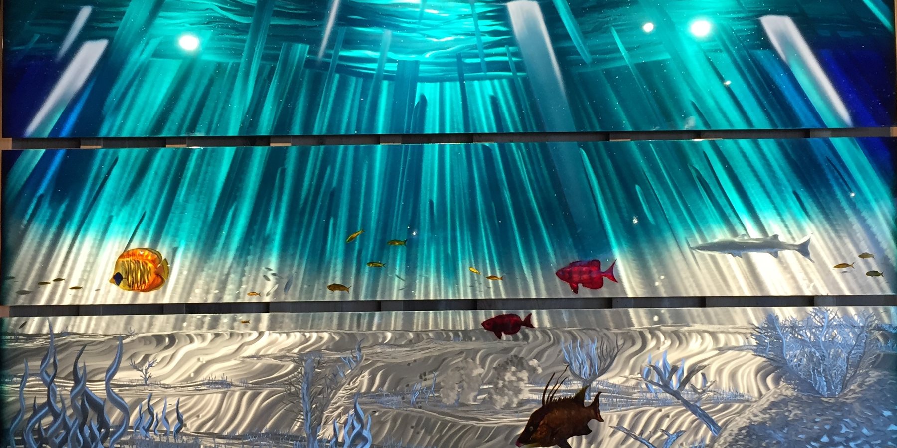 Metal relief triptych of a Florida Keys reef, turquoise light falling through the surface onto a sandy bottom with a shark, a hogfish and coral.