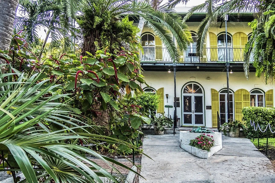 "Hemingway House - Key West" - the yellow-shuttered facade and veranda of the Hemingway House seen through palms and tropical planting