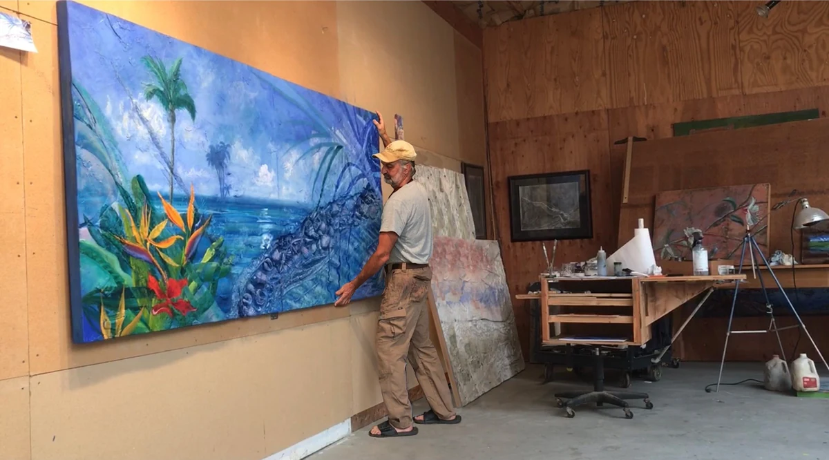 Dayton Claudio in his studio standing beside the finished Paradise 88.8 panel, one hand resting on it
