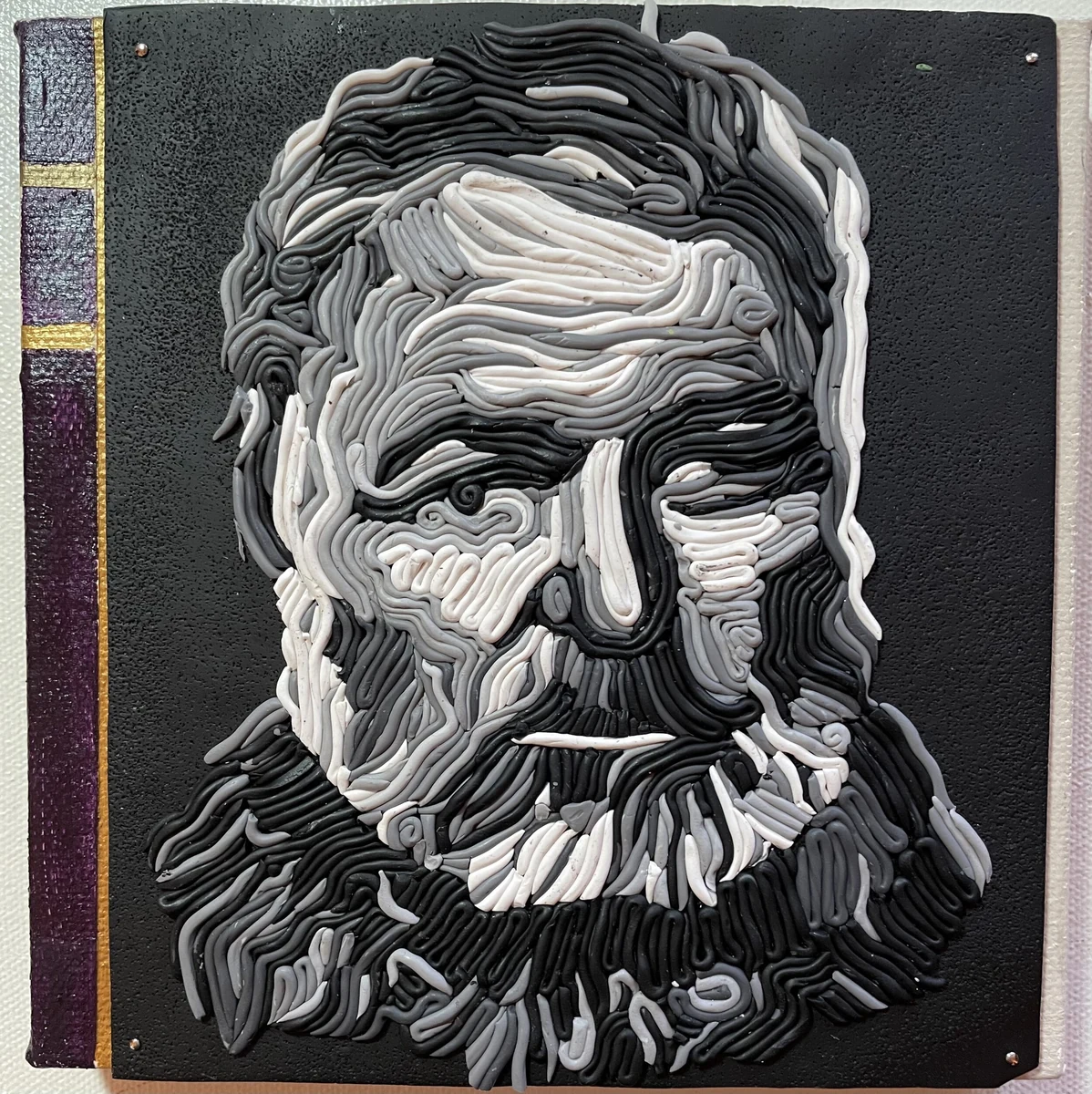 Black, white and gray polymer clay relief portrait of a bearded man (Hemingway), built from coiled strands of pigmented clay, with a book-spine panel down the left edge