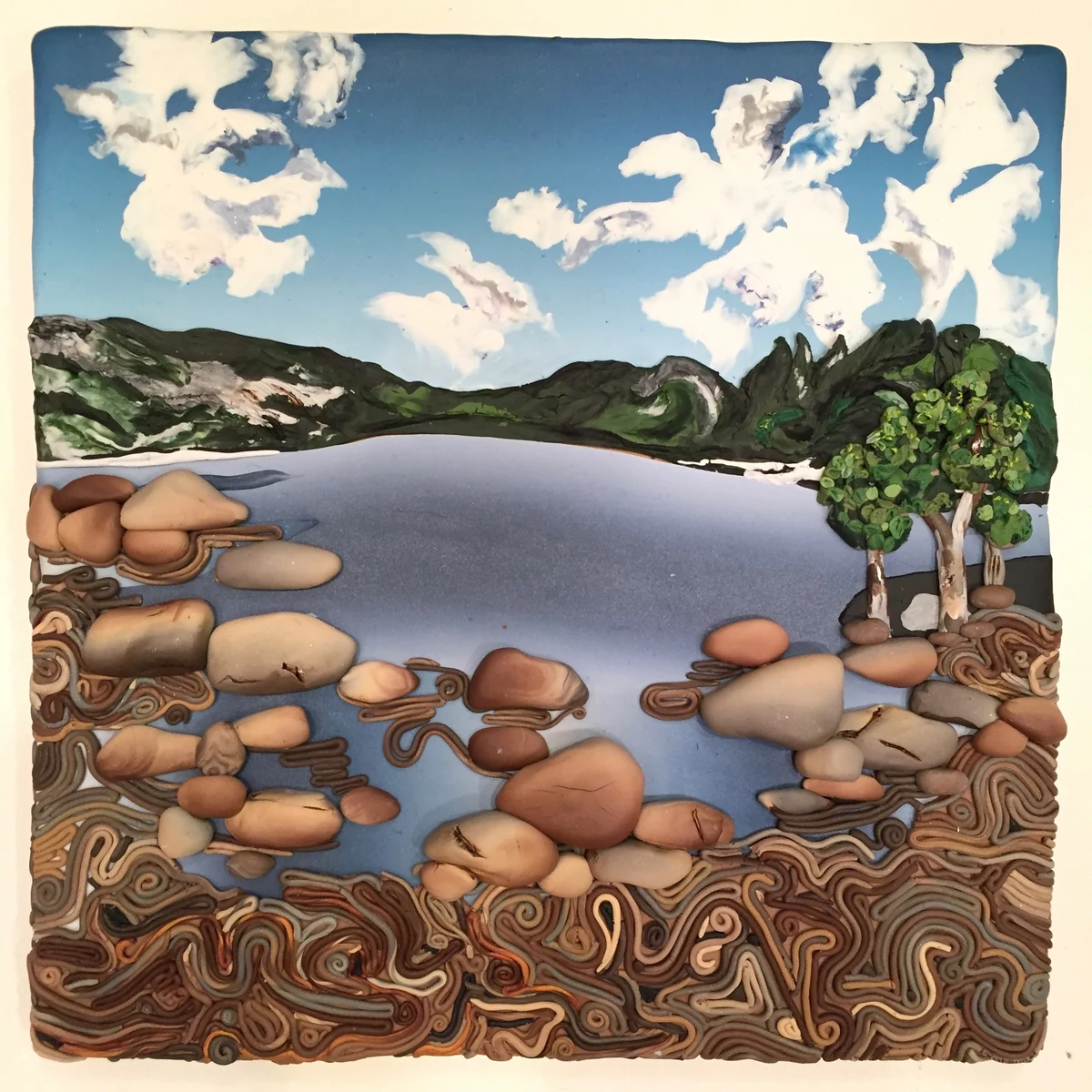 Dimensional polymer clay landscape of a still lake with scattered boulders, wooded hills and towering white clouds, the foreground worked in swirling marbled clay
