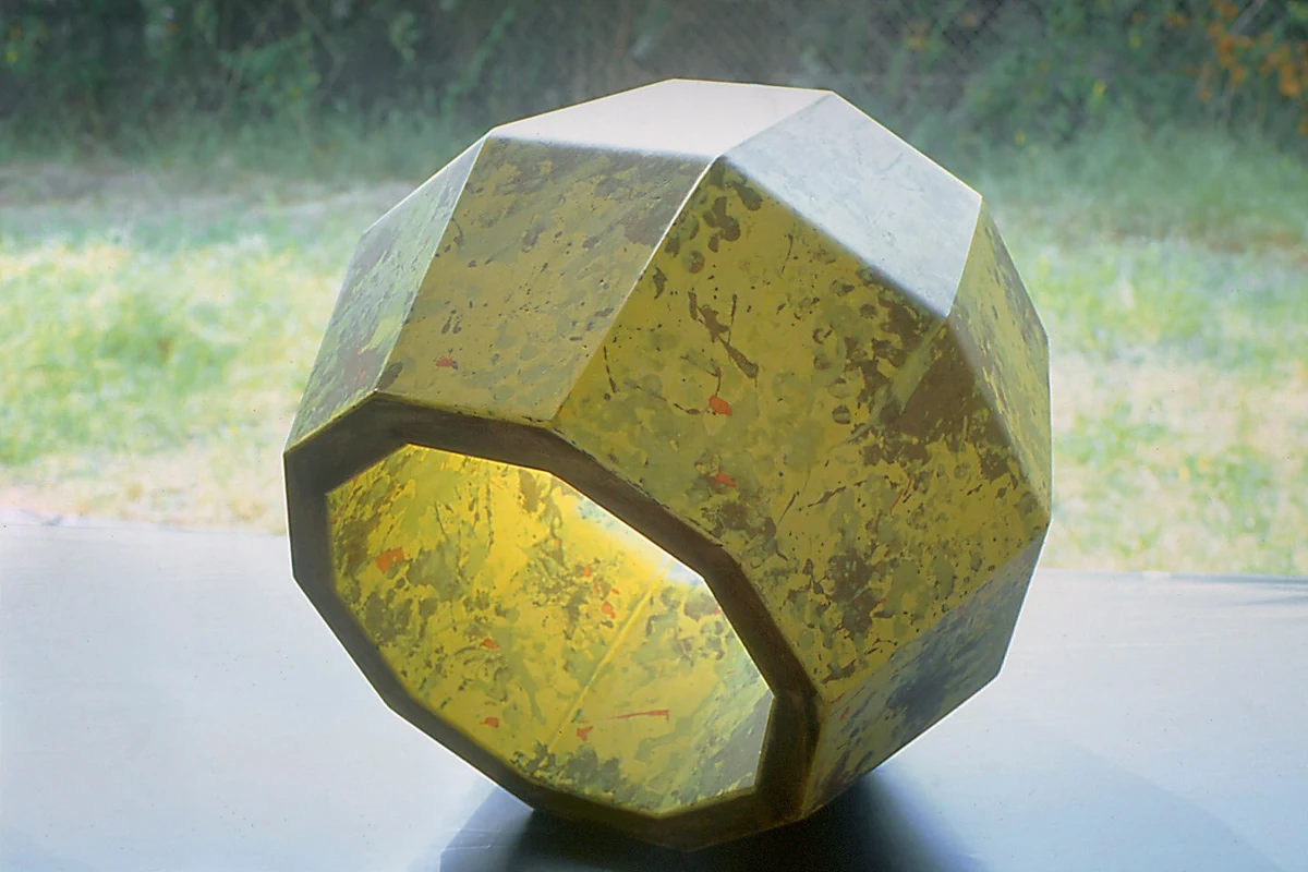 Tumble, resin-composite, 16 x 19 x 18 inches, 2005: a hollow faceted polyhedron with a mottled gold and green surface, photographed outdoors on a ledge