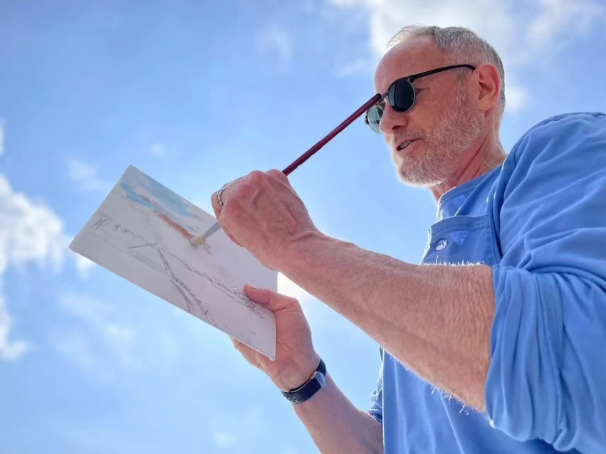 Larry Thimmesch painting a watercolor outdoors, brush in hand, against an open sky