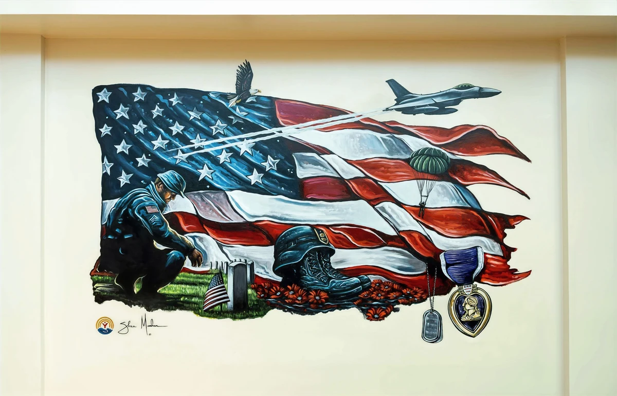 Memories of the Fallen mural: a kneeling soldier at a headstone before a torn American flag with an eagle, fighter jet, combat boots, dog tags and a Purple Heart