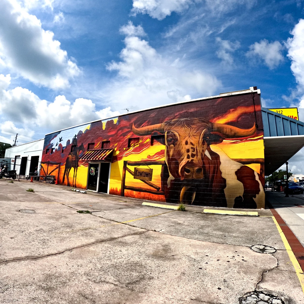 Kowtown mural in downtown Kissimmee: a longhorn bull and a mounted cowboy against a red and gold sunset, wrapping the corner of a brick building