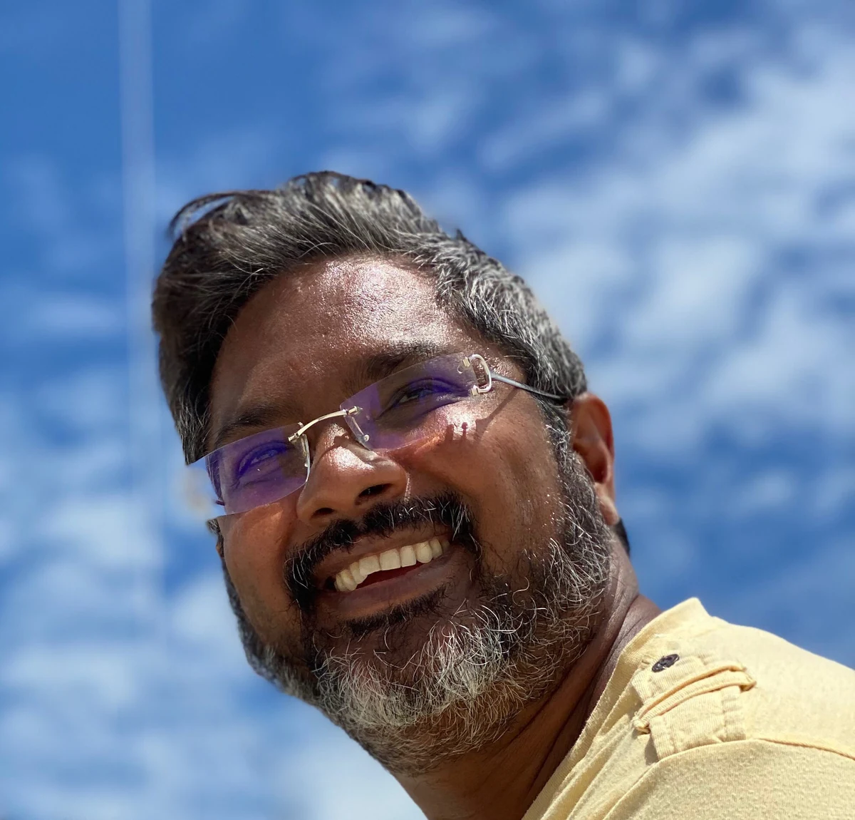 Shiva Maharaj, smiling, photographed from below against a blue sky
