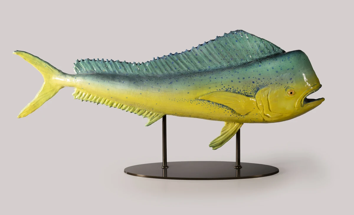 Mahi mahi sculpture in green, blue and yellow, mounted on a bronze rod stand against a plain studio background