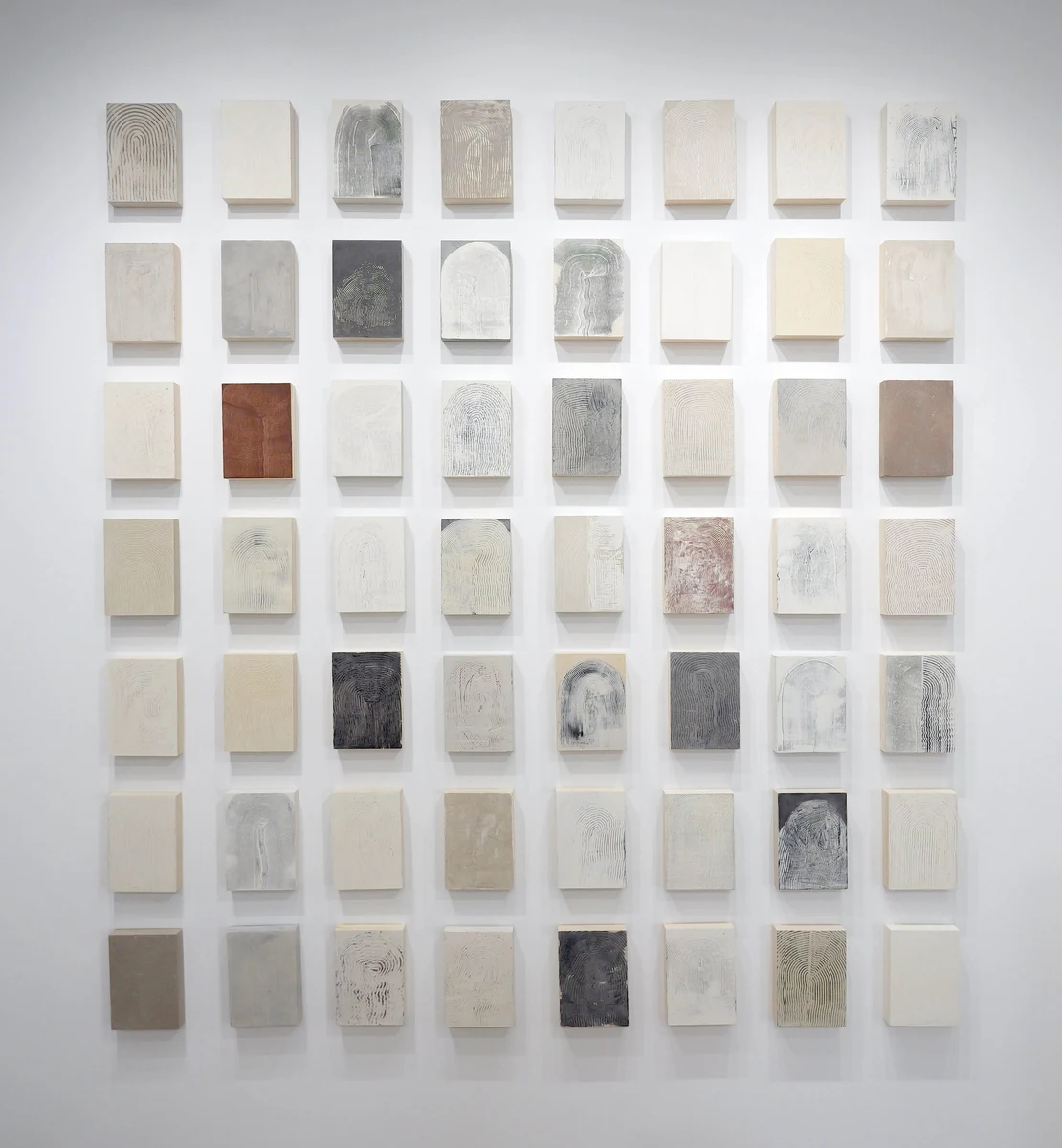 The Passage series installed as a grid of small mixed media panels in bone, gray and rust tones on a white wall