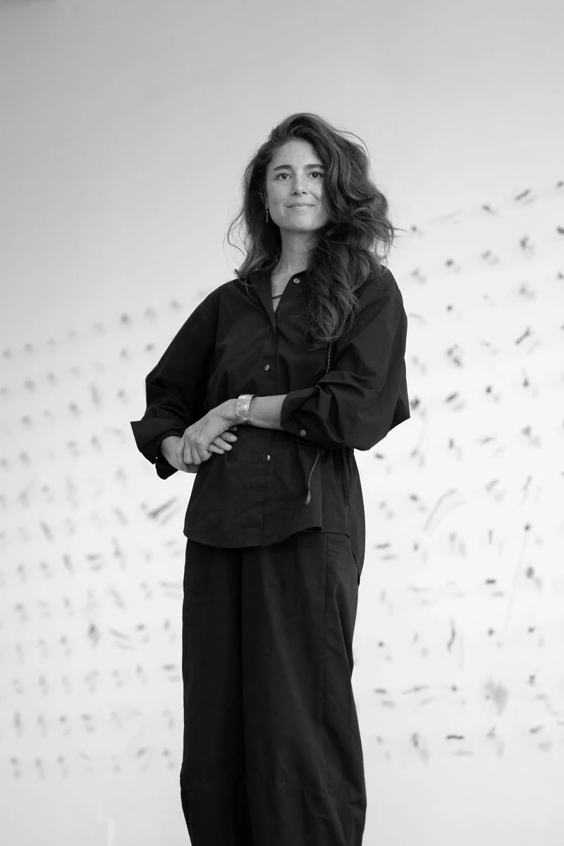Tory Mata standing in front of a wall of her small mark-making works, black and white portrait